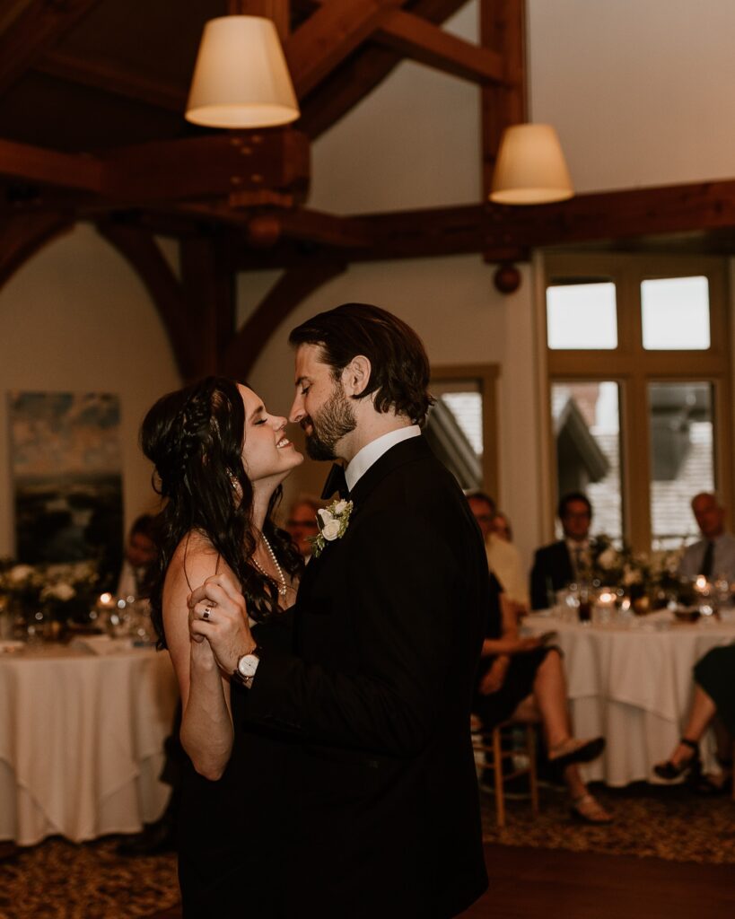 Vermont Wedding Venues | Sincerely Liz Photography Vermont Wedding Photographer | A couple shares a romantic dance at a wedding reception, gazing lovingly at each other. They are surrounded by elegantly set tables and guests.