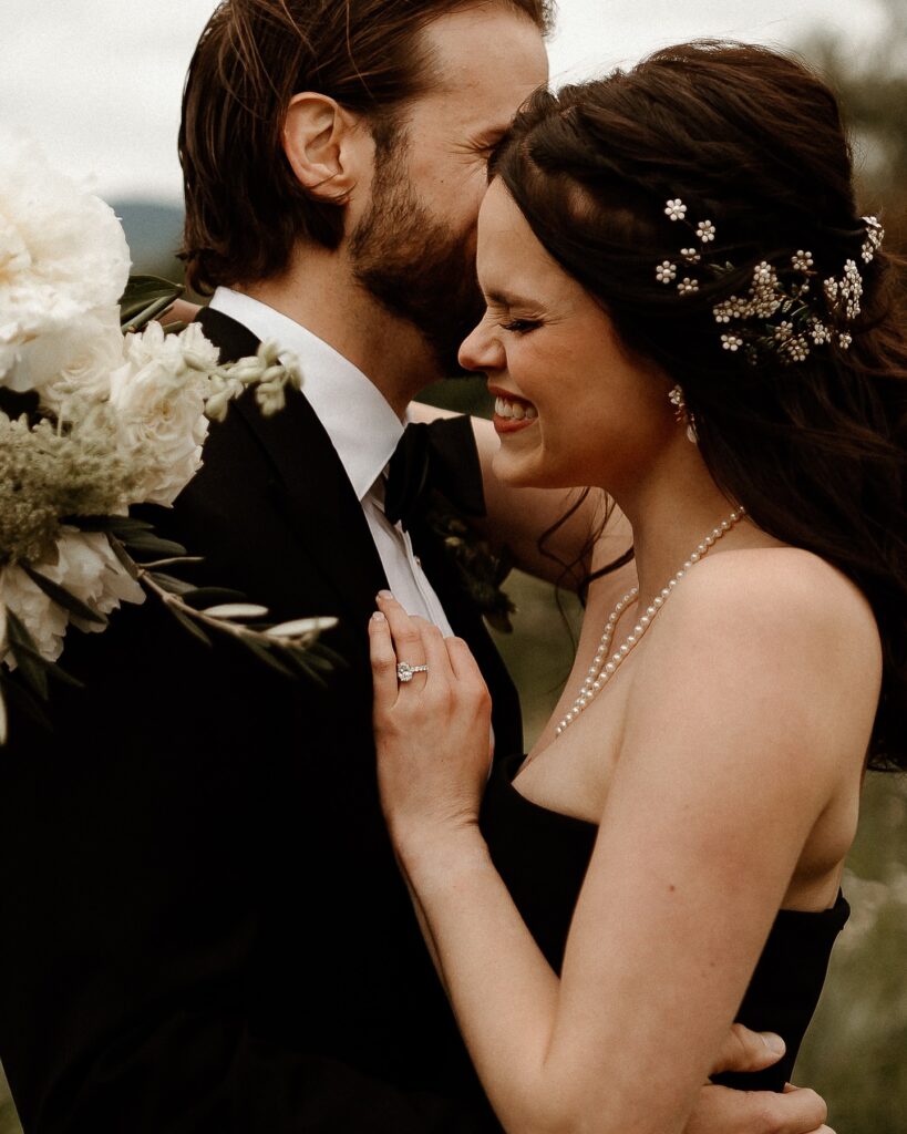 Vermont Wedding Venues | Sincerely Liz Photography Vermont Wedding Photographer | Bride and groom sharing an intimate embrace outdoors. The bride smiles with eyes closed, wearing a pearl necklace and floral hairpiece. Romantic and joyful atmosphere.