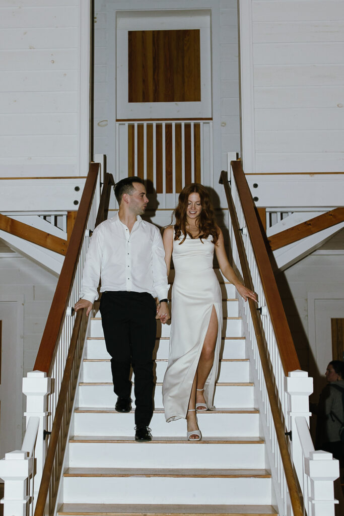 The couple descends a white wooden staircase together in evening attire, a polished detail from a wedding in Vermont.