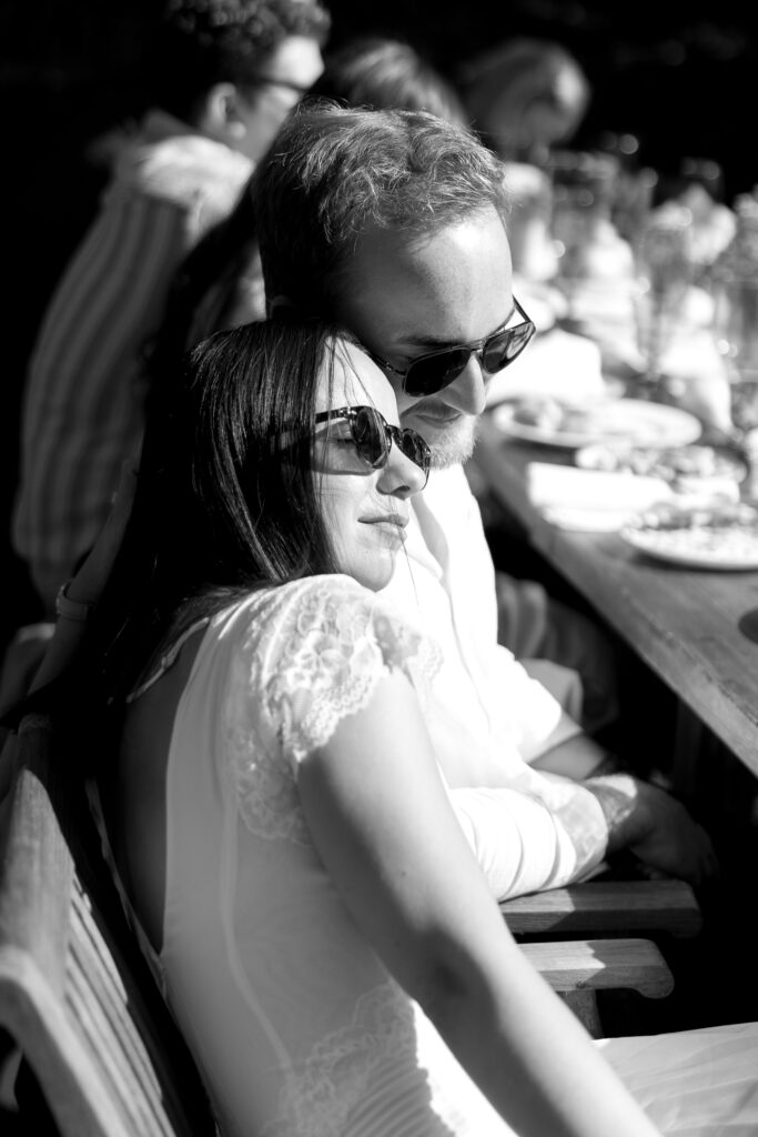 Black-and-white photograph of a couple leaning into each other during dinner, preserving an unposed connection through documentary Vermont wedding photography.