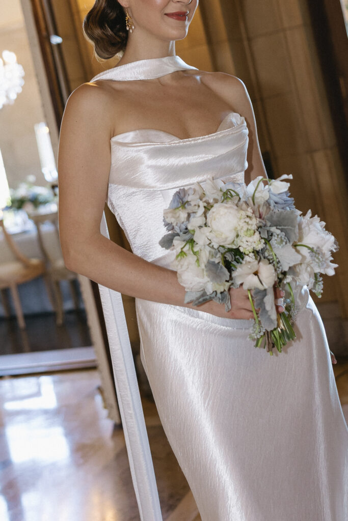 Bride holding a soft white bouquet in a sleek satin gown, photographed with natural color and an editorial approach by a Vermont wedding photographer.
