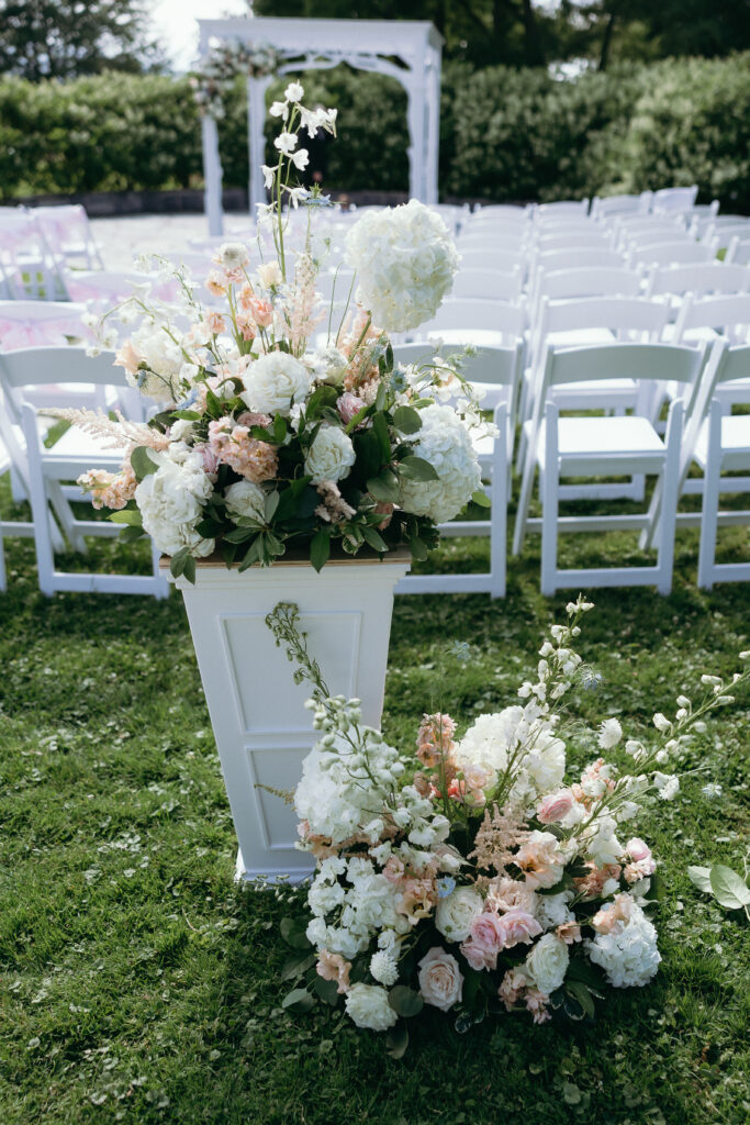 Vermont Wedding Venues | Sincerely Liz Photography Vermont Wedding Photographer | Outdoor wedding setup with white chairs arranged in rows on grass. Elegant floral arrangements with white and pastel flowers decorate the aisle.