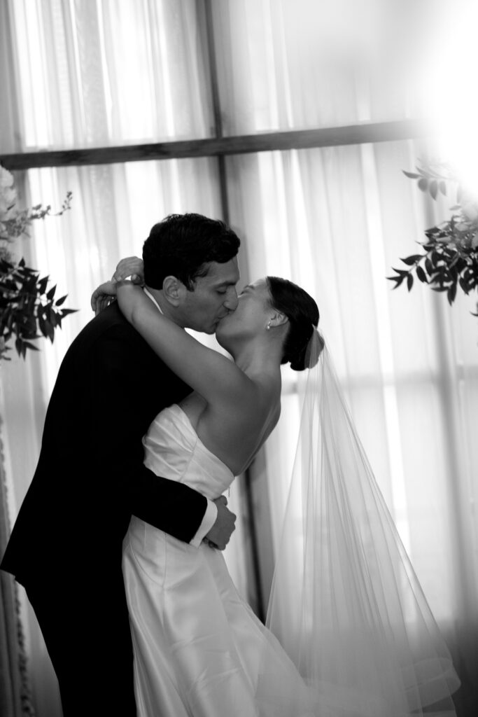 A black-and-white portrait shows the newlyweds kissing near soft drapery, a timeless image from wedding photography in VT.