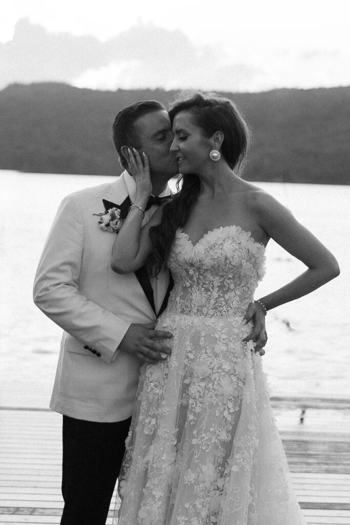 Black-and-white portrait of newlyweds sharing a kiss beside the water, an intimate moment that reflects the emotion of documentary wedding photography in Vermont.