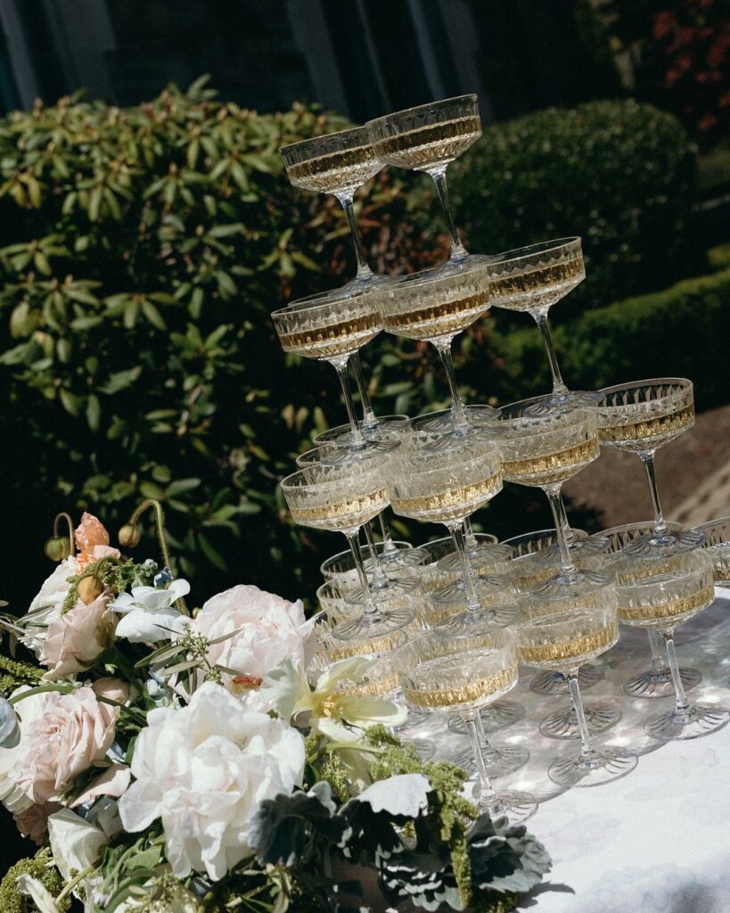 A champagne tower glows beside soft white florals, adding an elegant reception detail to a wedding in VT.