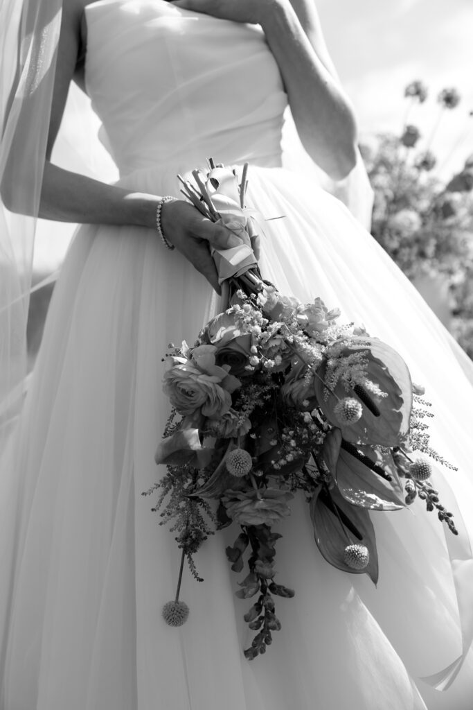 Inn by the Sea Maine | Sincerely Liz Photography Documentary and Editorial Wedding Photography | A bride in a flowing gown holds a bouquet of flowers. The black-and-white image captures an elegant and serene atmosphere, highlighting bridal details.
