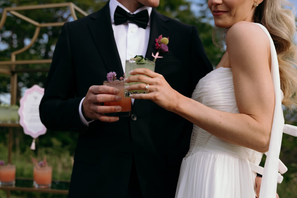 The couple holds cocktails close together in a tailored close-up with floral details and black tie styling, a polished reception moment at a Vermont wedding venue for a smaller celebration.