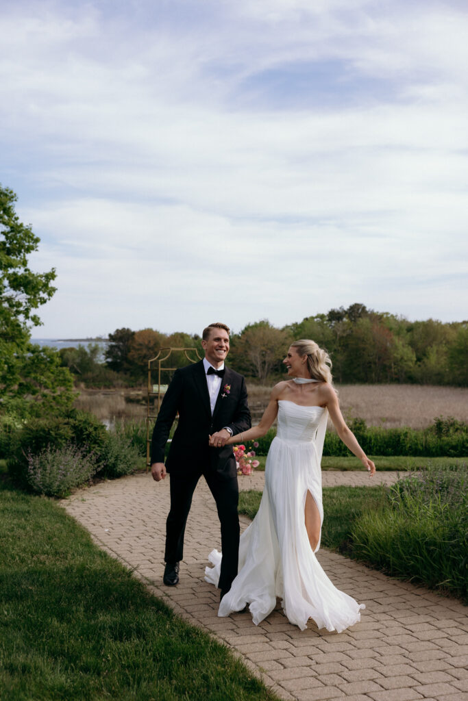 Walking along a garden path, the couple looks back at each other under a wide sky, reflecting the relaxed beauty of a Vermont destination wedding.