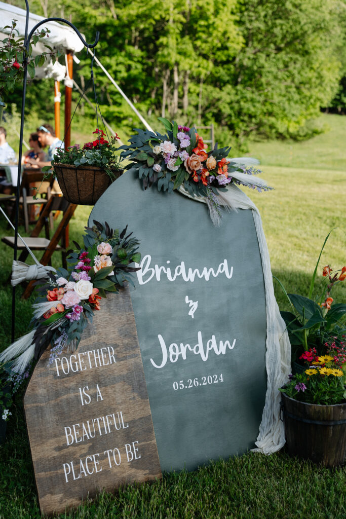 A hand-lettered welcome sign surrounded by flowers stands on the lawn before the celebration begins, a charming entrance moment for best small wedding venues in Vermont.