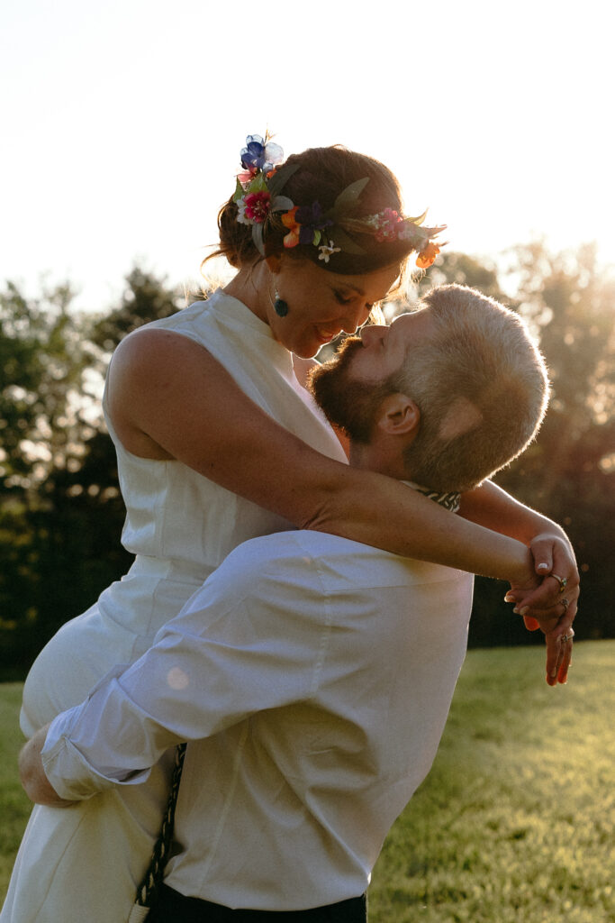 A bride in a floral crown wraps her arms around her partner in warm sunset light, a romantic portrait from one of the best Vermont wedding venues.