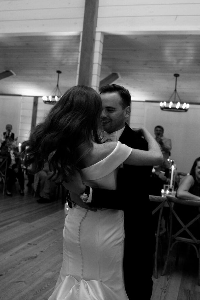 Vermont Wedding Photographer | Sincerely Liz Photography Documentary and Editorial Wedding Photography | A couple shares a romantic embrace on the dance floor during a wedding reception. They smile warmly, surrounded by seated guests and soft candlelight.