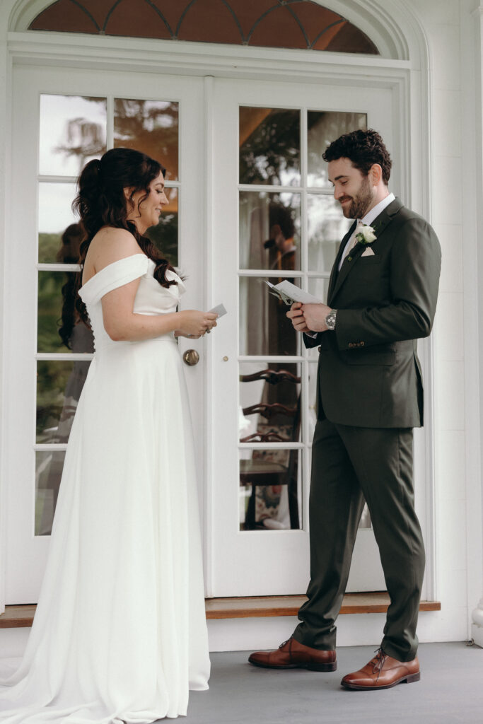 Smith Farm Gardens Wedding | Sincerely Liz Photography Documentary and Editorial Wedding Photography | Bride in an off-shoulder white gown and groom in a dark suit exchange vows in front of elegant, arched white doors, conveying joy and romance.