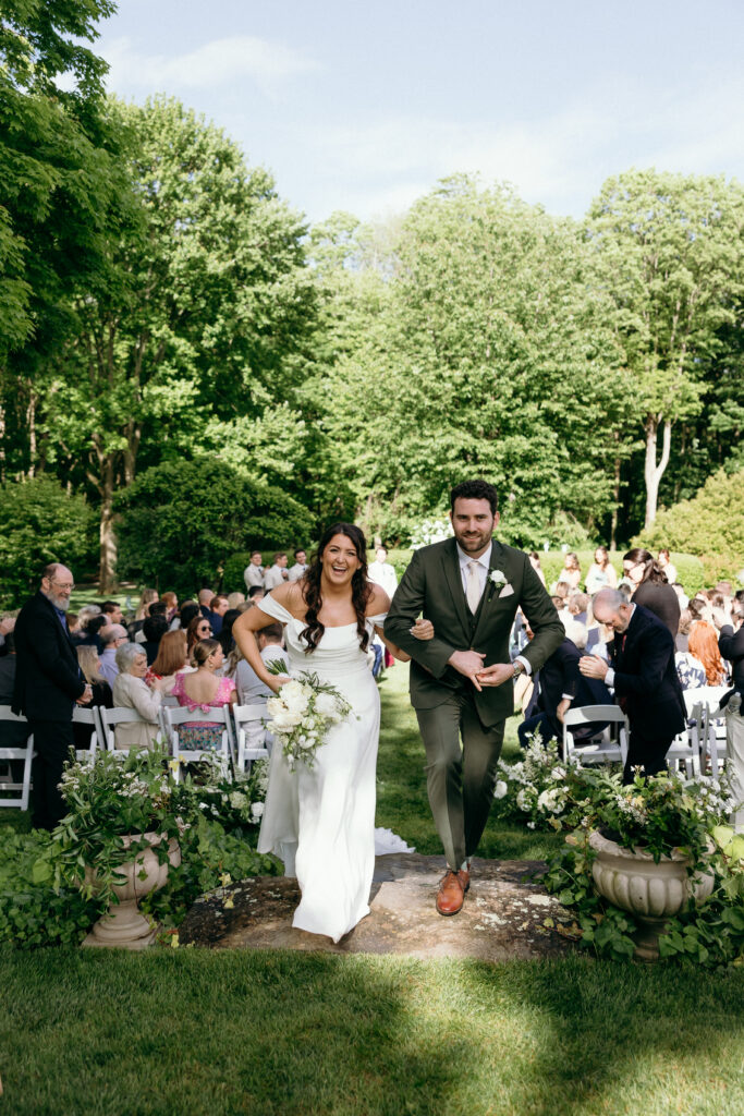The bride and groom walk back down the aisle together, smiling as guests celebrate around them in a garden setting at Smith Farm Gardens.