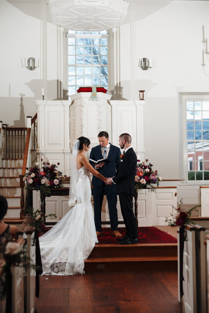 Wedding Photographer VT | Sincerely Liz Photography Documentary and Editorial Wedding Photography | Bride and groom in elegant attire exchange vows in a bright church, with a pastor officiating.