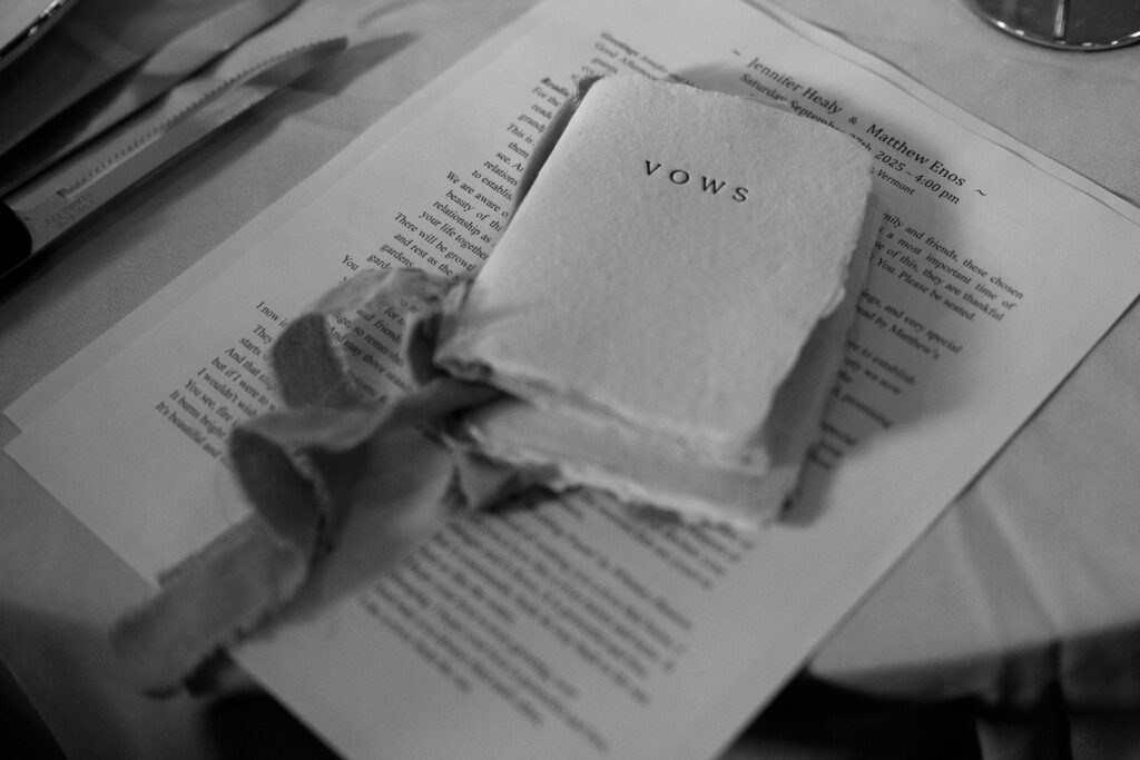 Wedding Photographer in Vermont | Sincerely Liz Photography Documentary and Editorial Wedding Photography | Black and white image of a book titled "Vows" with worn pages and a ribbon, lying on a printed document. It conveys a nostalgic and intimate tone.