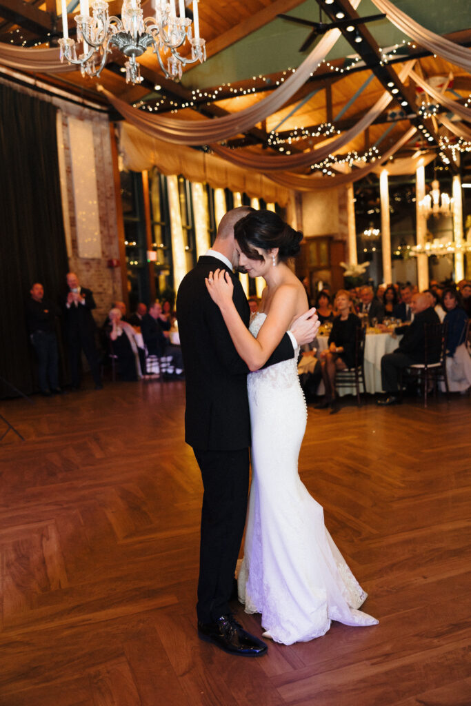 Wedding Photographer in Vermont | Sincerely Liz Photography Documentary and Editorial Wedding Photography | A couple shares a tender embrace during their first dance at a wedding reception. The venue is elegantly decorated with draped fabric and twinkling lights, creating a romantic ambiance.