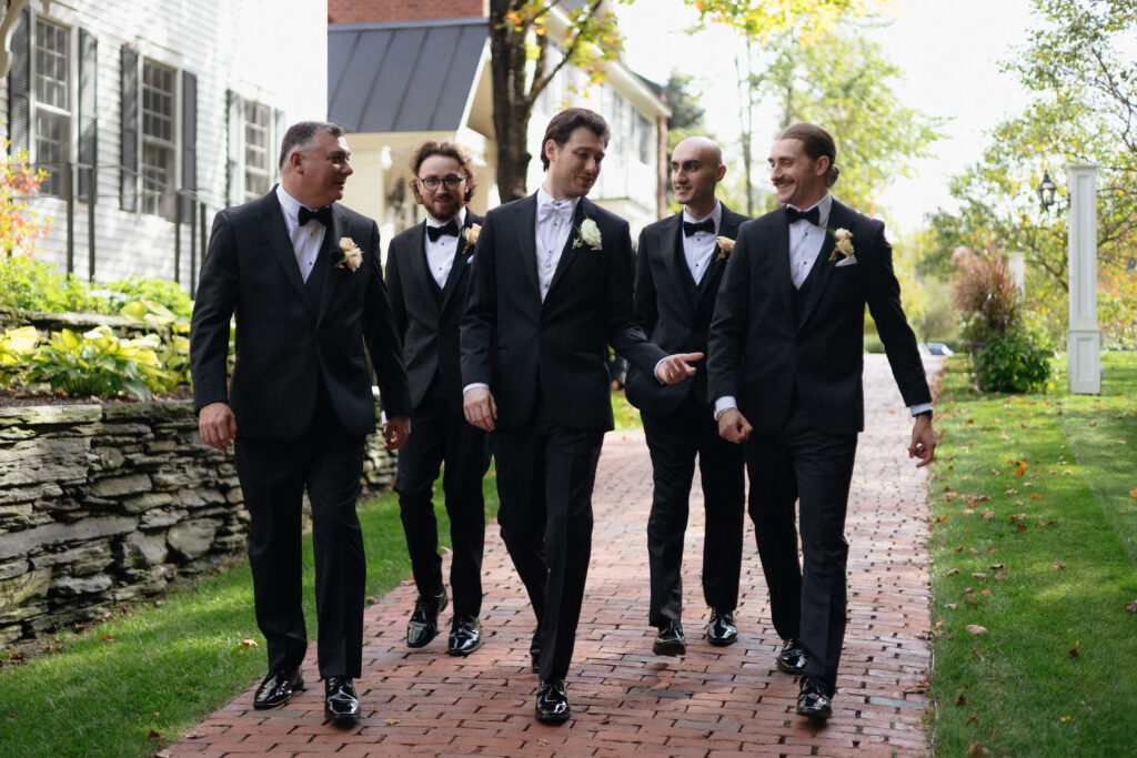A group of groomsmen walk together along a brick pathway in tailored suits, adding a refined and social element often seen at top Vermont wedding venues.