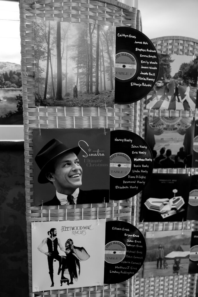 Wedding Photographer VT | Sincerely Liz Photography Documentary and Editorial Wedding Photography | Black and white photo of woven display stand featuring album covers of Frank Sinatra and Fleetwood Mac, with vinyl records listing names and nature scene postcards. Retro, nostalgic tone.