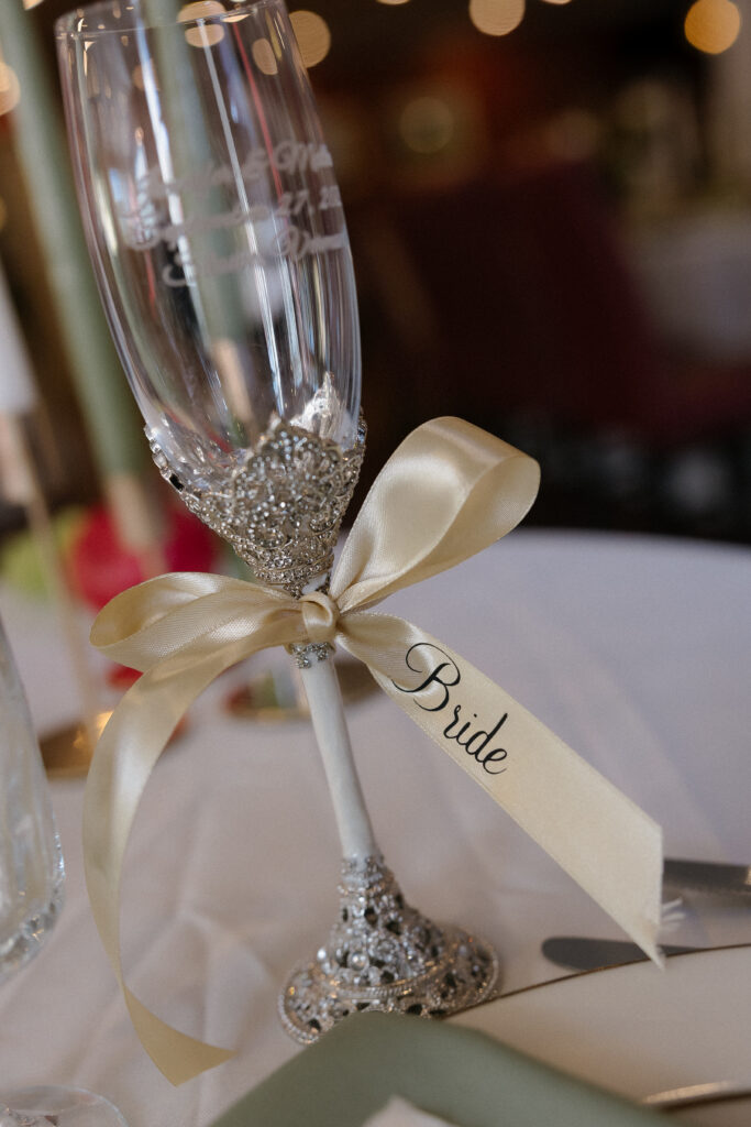 Crystal champagne flute tied with a satin ribbon labeled “Bride” photographed during reception details, adding a romantic close-up often included in artistic wedding photography VT coverage.