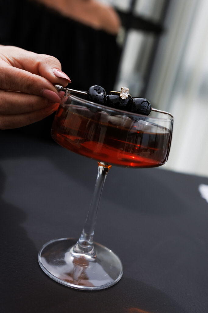 A hand garnishes a deep red cocktail in a coupe glass, a refined reception moment that fits wedding weekend venues VT.