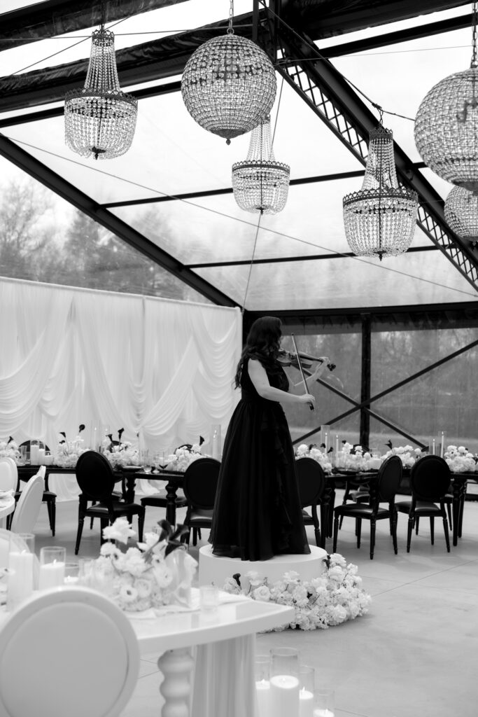 Musician performs beneath a glass reception structure in a black-and-white documentary-style image that highlights the architectural atmosphere of The Hacienda wedding photography.