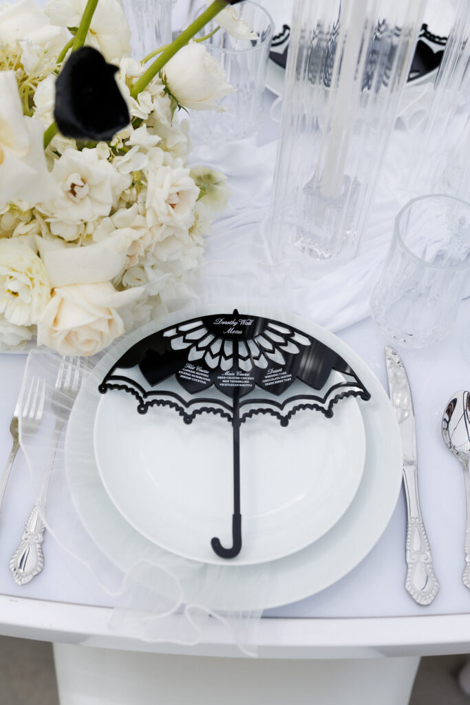 Black lace umbrella detail rests on layered white dinnerware surrounded by florals and crystal glassware, capturing the romantic styling woven throughout this Massachusetts styled wedding shoot.