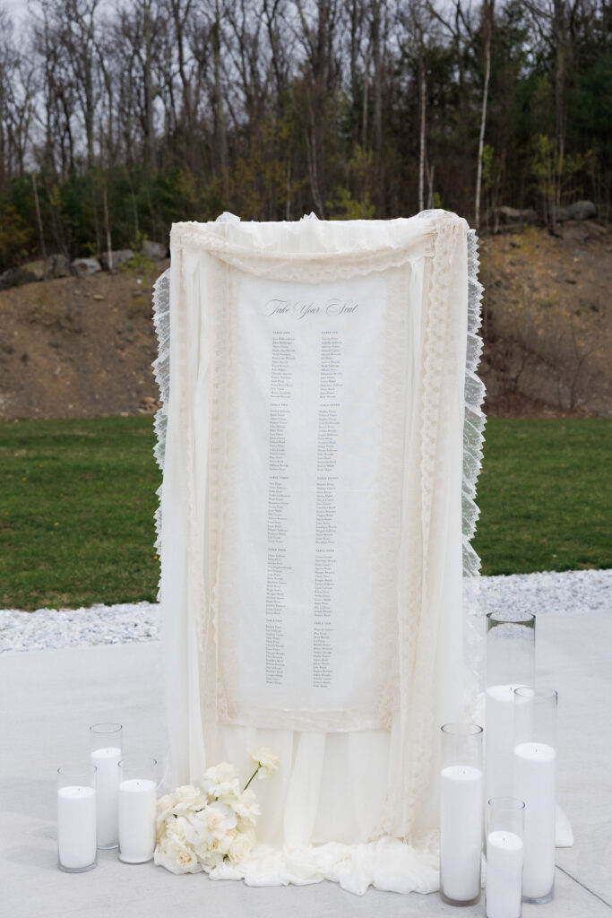 Minimalist seating chart display framed with soft fabric and candles set outdoors before the ceremony, photographed with the intentional styling often seen in editorial wedding photographers in Vermont portfolios.