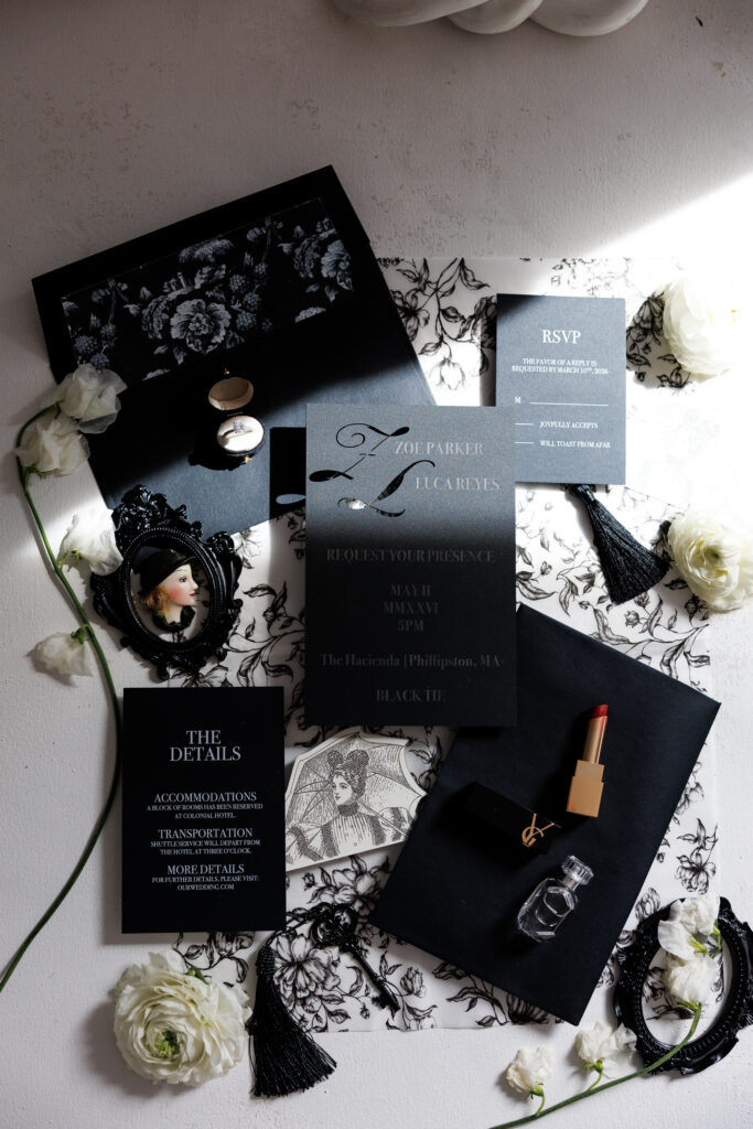 Editorial flat lay of black-and-white invitation suites, florals, ribbon, and bridal accessories styled for a luxury Massachusetts wedding inspiration gallery.