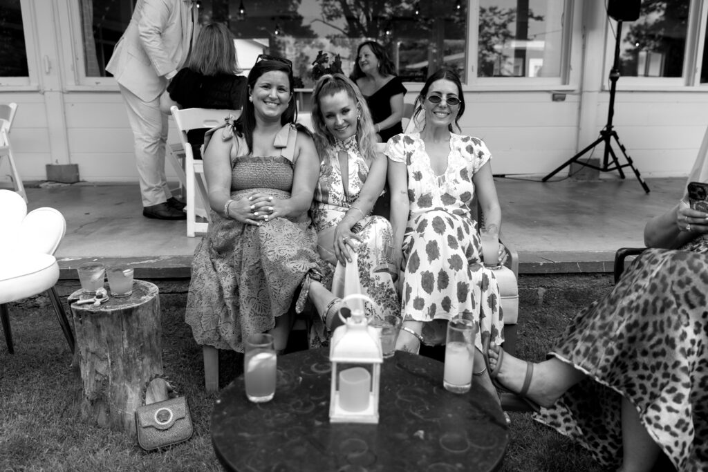 Black-and-white candid photograph of three wedding guests smiling together at Basin Harbor