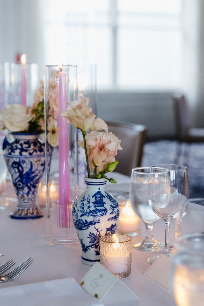 Pink taper candles, peach flowers, and blue-and-white vases decorating a Basin Harbor wedding reception table