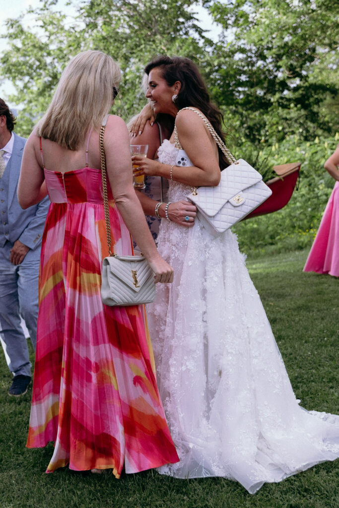 Candid moment between the bride and a guest in a colorful pink dress during a Basin Harbor wedding