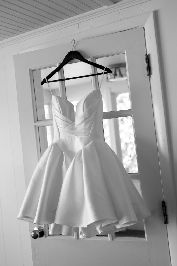 Short white satin wedding dress with a structured bodice hanging on a door at Basin Harbor