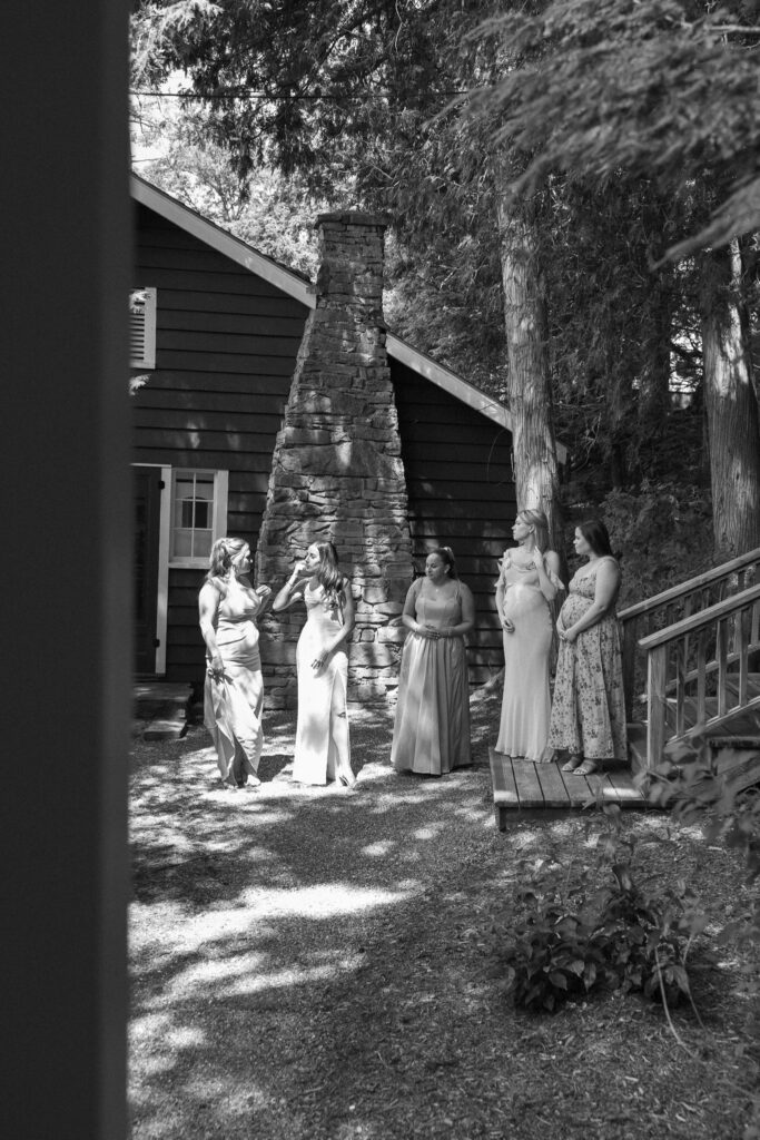 Black-and-white candid photograph of wedding party members gathered outside a rustic building at Basin Harbor
