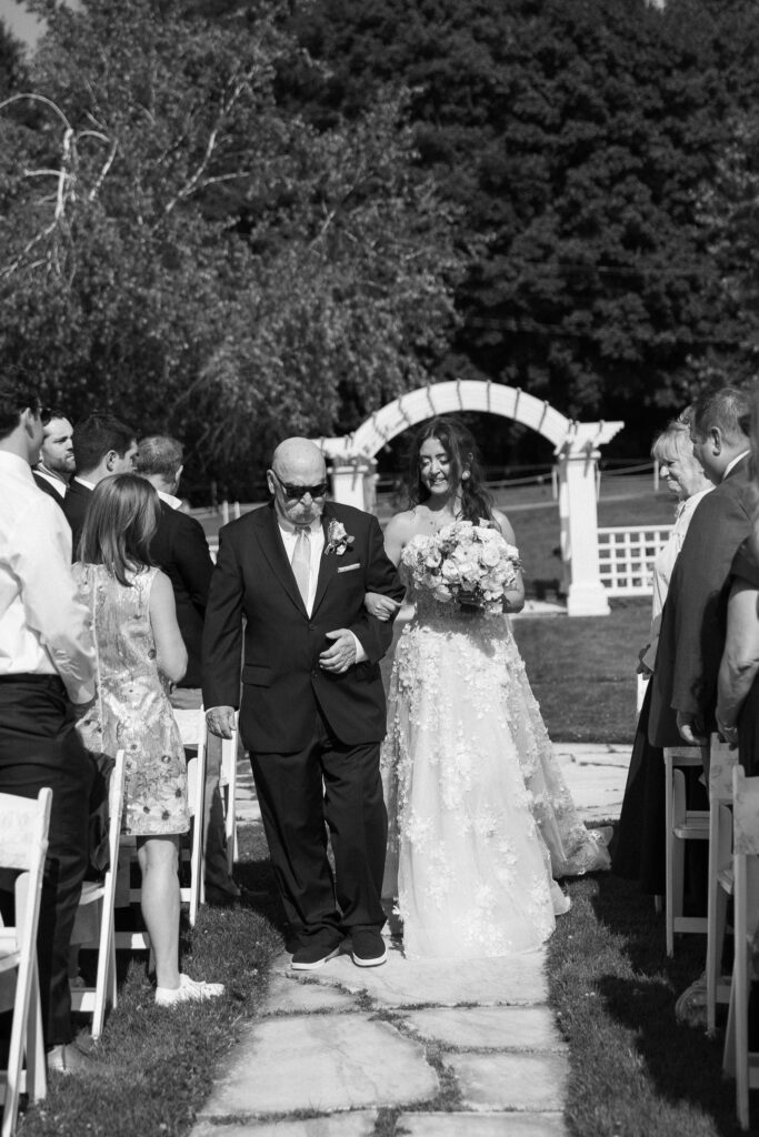 Bride walking down the outdoor ceremony aisle with her father at a Basin Harbor wedding