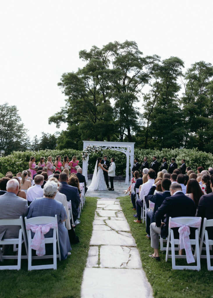 Basin Harbor wedding ceremony on a green lawn with white chairs, a floral arch, and guests