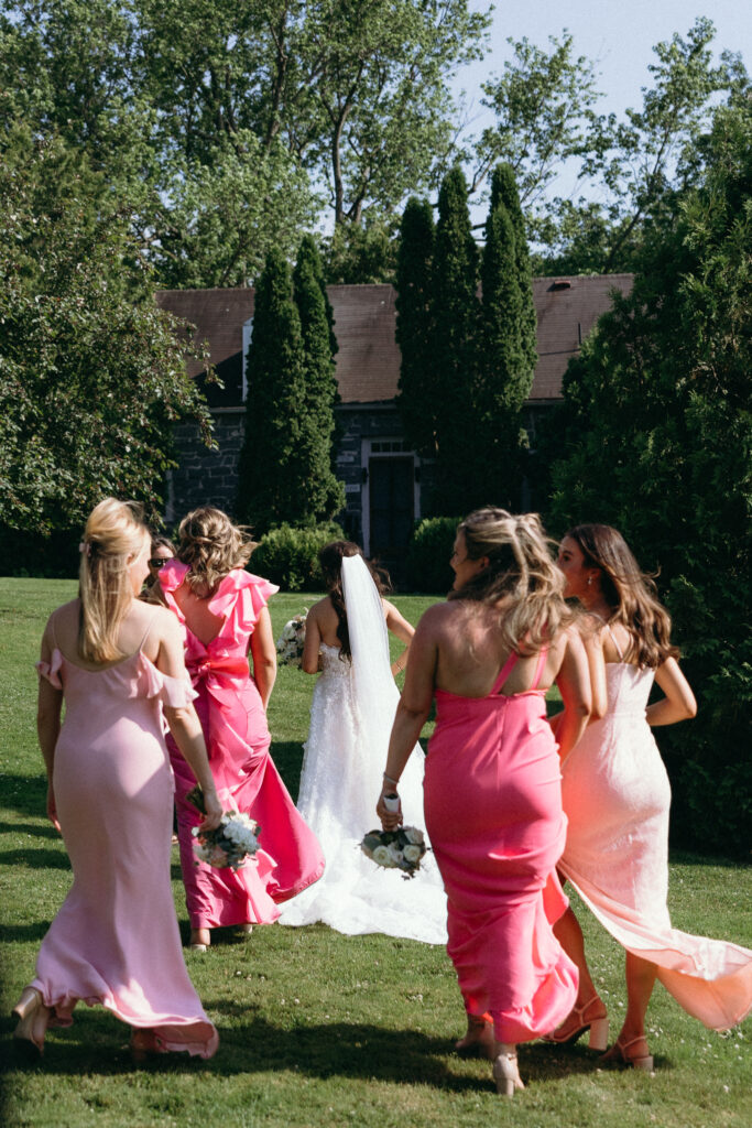 Bride walking across the lawn with her wedding party in colorful pink dresses at Basin Harbor