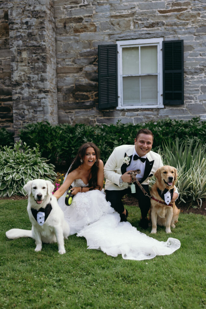 Newlyweds posing with two dogs beside a stone building during their Basin Harbor wedding