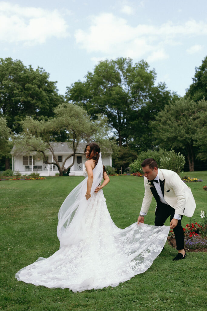 Groom arranging the bride's wedding dress train on the lawn at Basin Harbor
