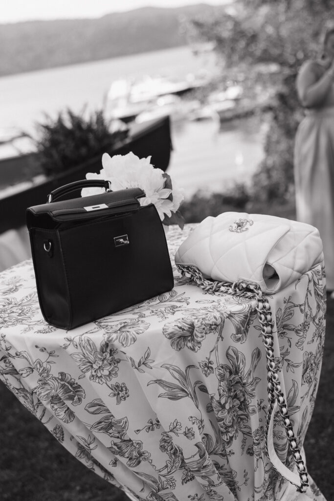Black-and-white photograph of a black handbag and white accessories arranged on a patterned tablecloth