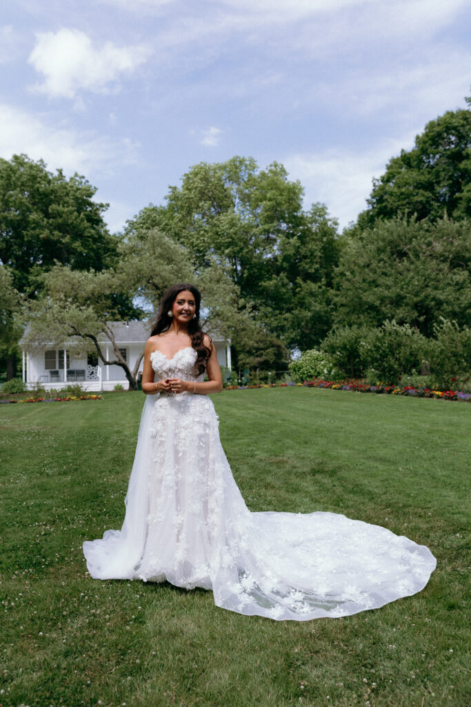 Bride posing in a white lace wedding gown on the green lawns of Basin Harbor in Vermont