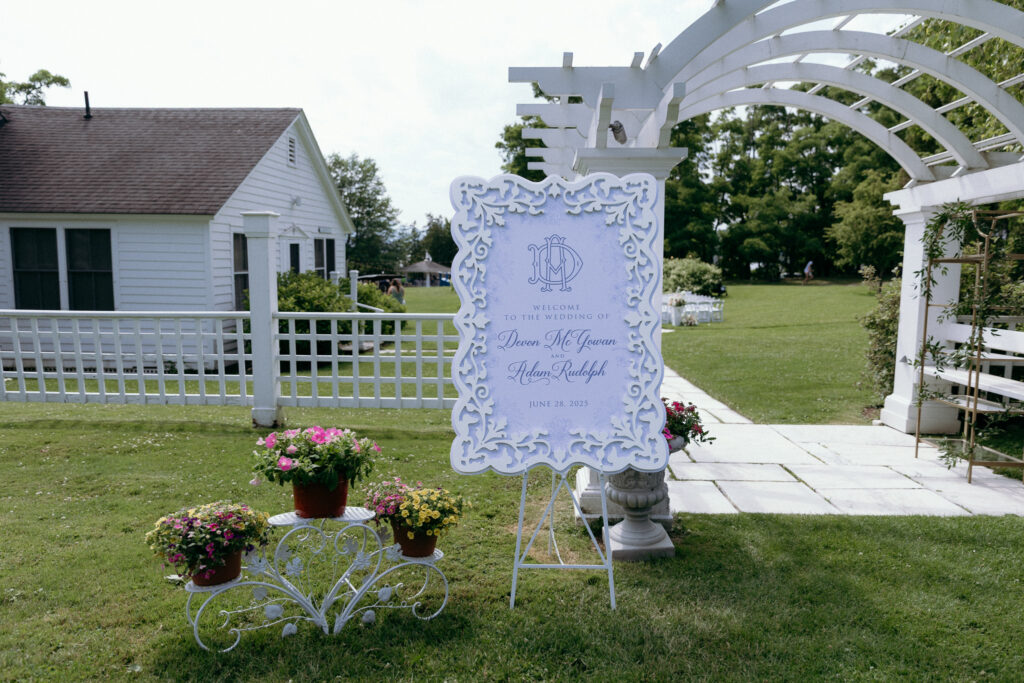Ornate white wedding welcome sign with pale blue lettering and floral accents outside at Basin Harbor