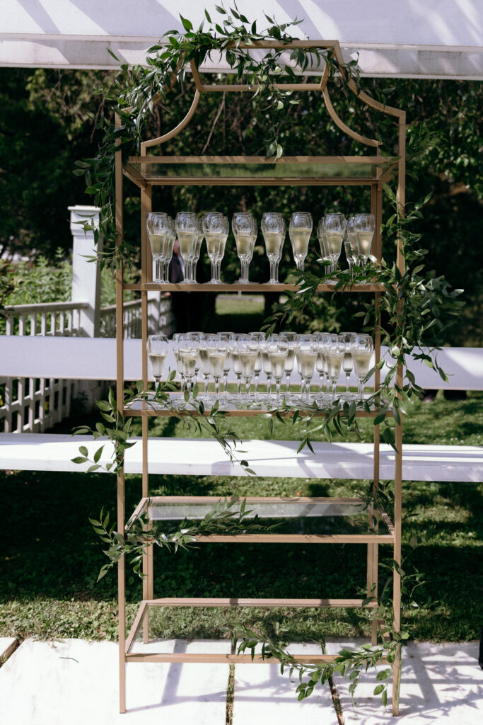 Gold champagne display decorated with greenery beneath a white tent at a Basin Harbor wedding